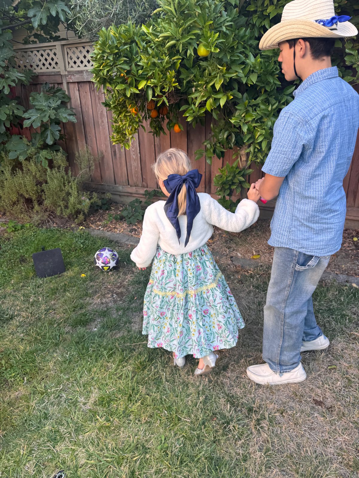 CJ in a straw hat holding hands with a little girl in a garden